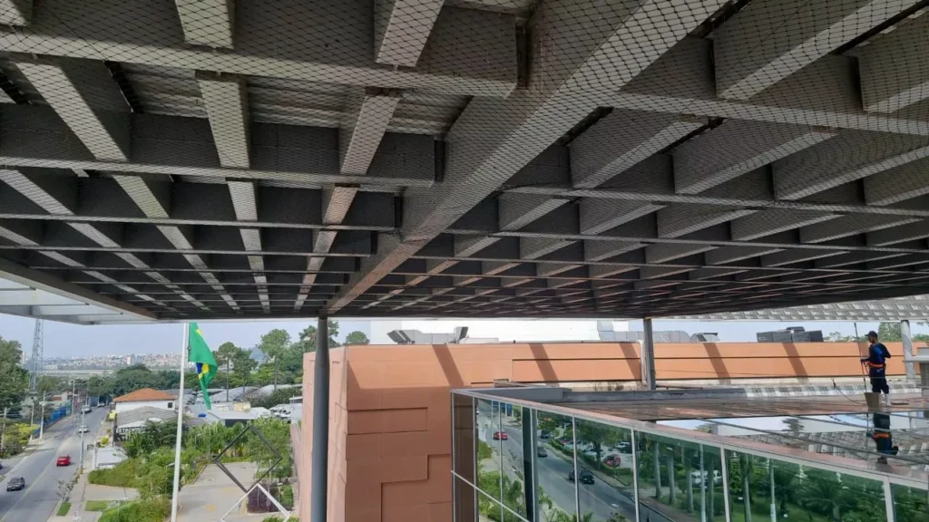 Rede de proteção instalada em telhado de galpão industrial para controle de pombos.